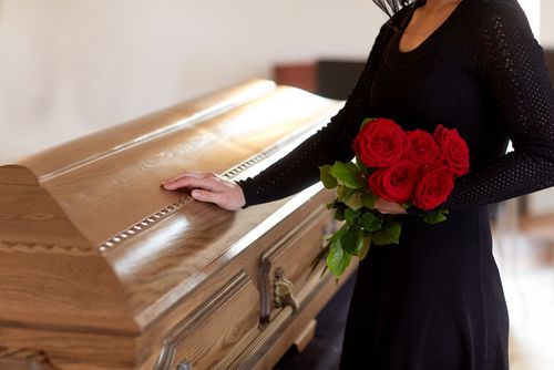 Woman With Flowers Standing in Front of a Coffin